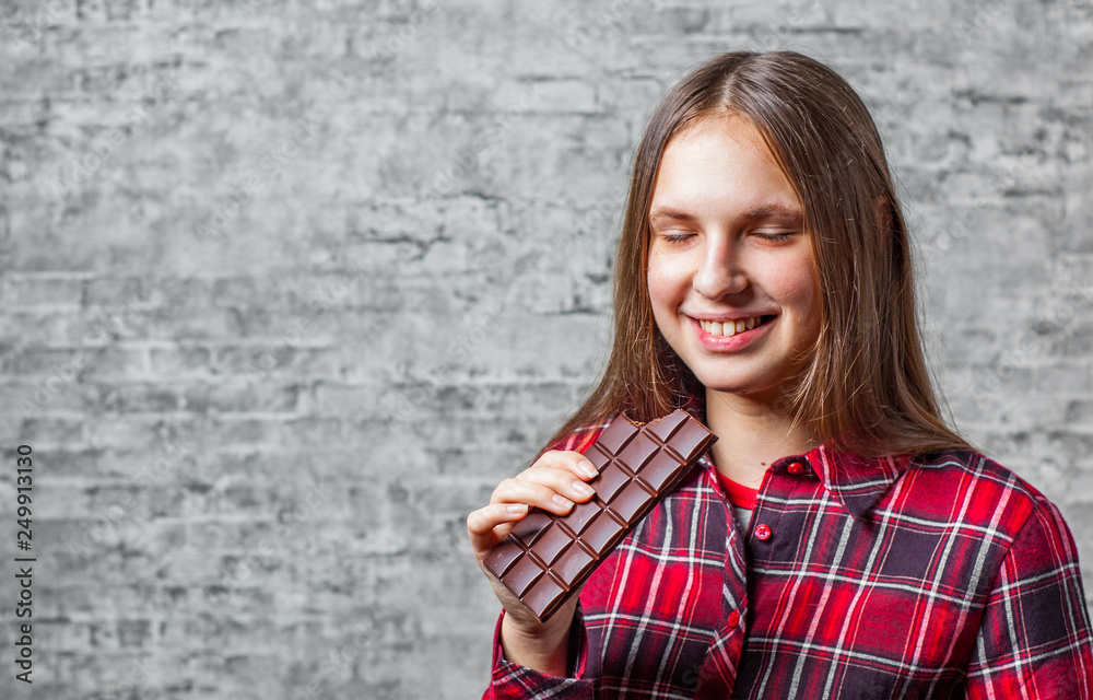 portrait of young teenager brunette girl with long hair eating chocolate on gray wall background portrait of young teenager brunette girl with long hair eating chocolate on gray wall background