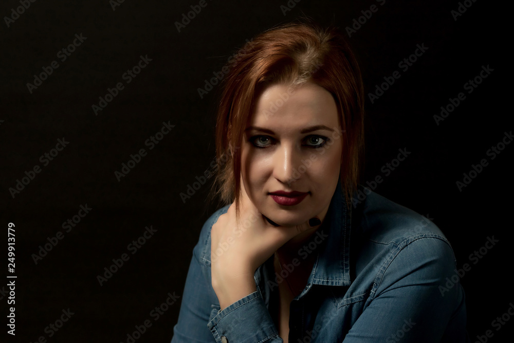 Low key portrait of pensive young woman looking at the camera on the black background. 