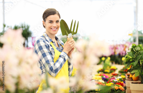 smiling woman in garden of flowers with garden tools, spring concept