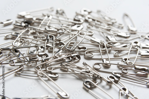 An extreme close-up or macro shot with selective focus on a bunch of safety pins in different sizes set on a white background.