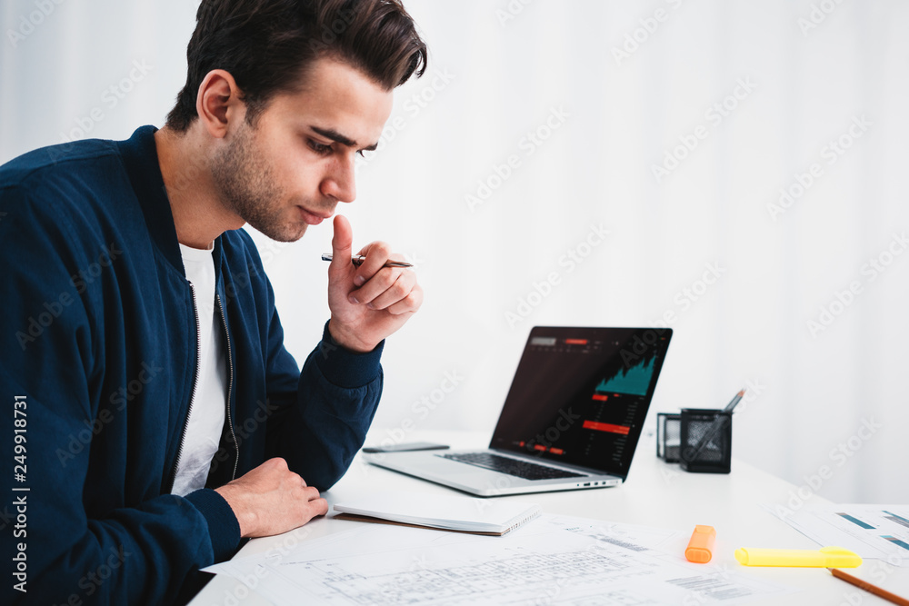 Businessman analyzing trends on screen laptop in space office. Male manager sitting at desktop and monitoring statistics on monitor Businessman analyzing trends on screen laptop in space office. Male manager sitting at desktop and monitoring statistics on monitor