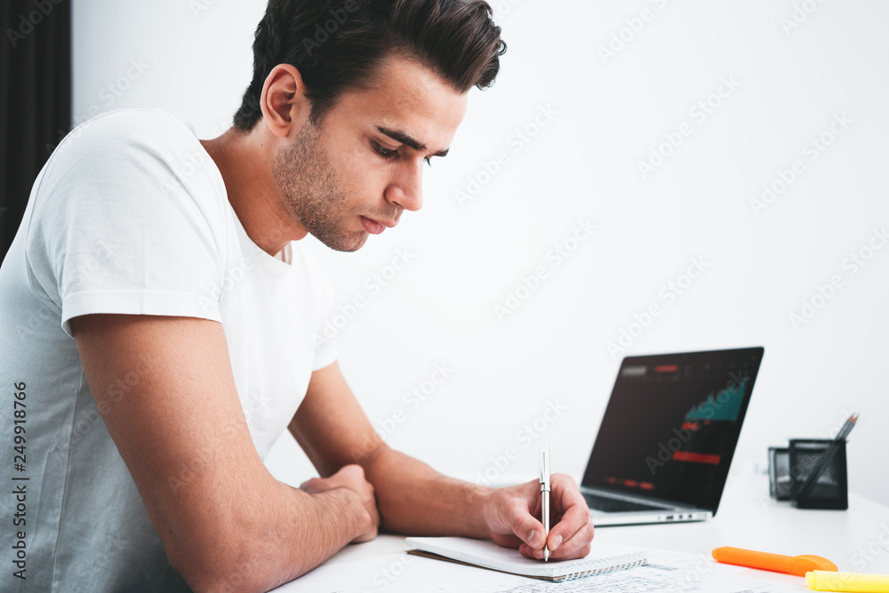 Project designer preparing creative smart building and laptop with digital graphs and notepad sitting by the table in office. Businessman analyzing trends on screen monitor and makes working plan Project designer preparing creative smart building and laptop with digital graphs and notepad sitting by the table in office. Businessman analyzing trends on screen monitor and makes working plan