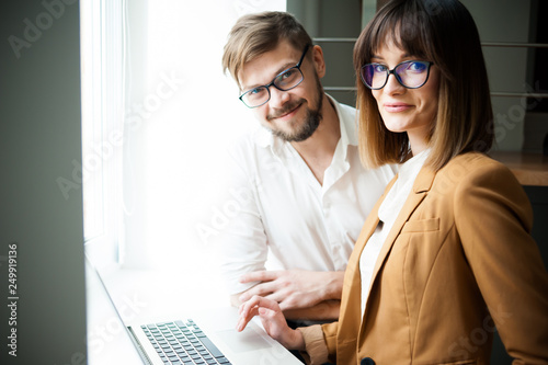 Two young coworkers dressed casual using laptop in white interior