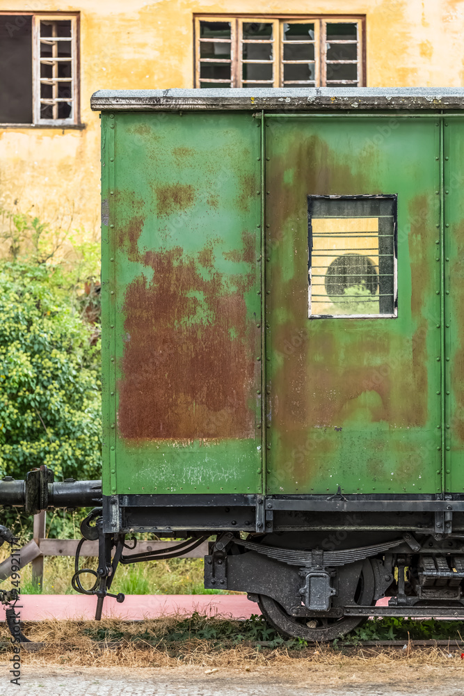 View of a abandoned and older rustic train wagon, yellow building as background