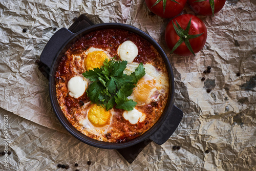 Shakshuka with eggs, tomatoes and parsley in a frying pan, close-up