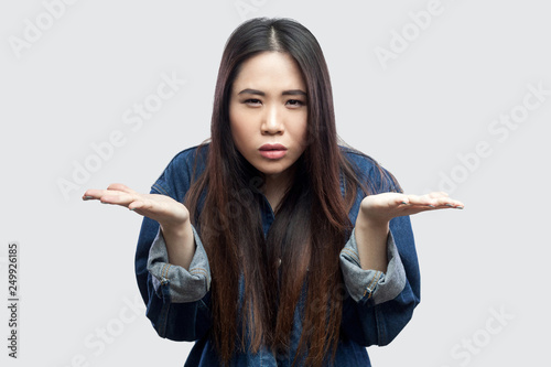 what do you want? Portrait of anger beautiful brunette asian young woman in casual blue denim jacket with makeup standing raised arms and asking. indoor studio shot, isolated on light grey background. photo