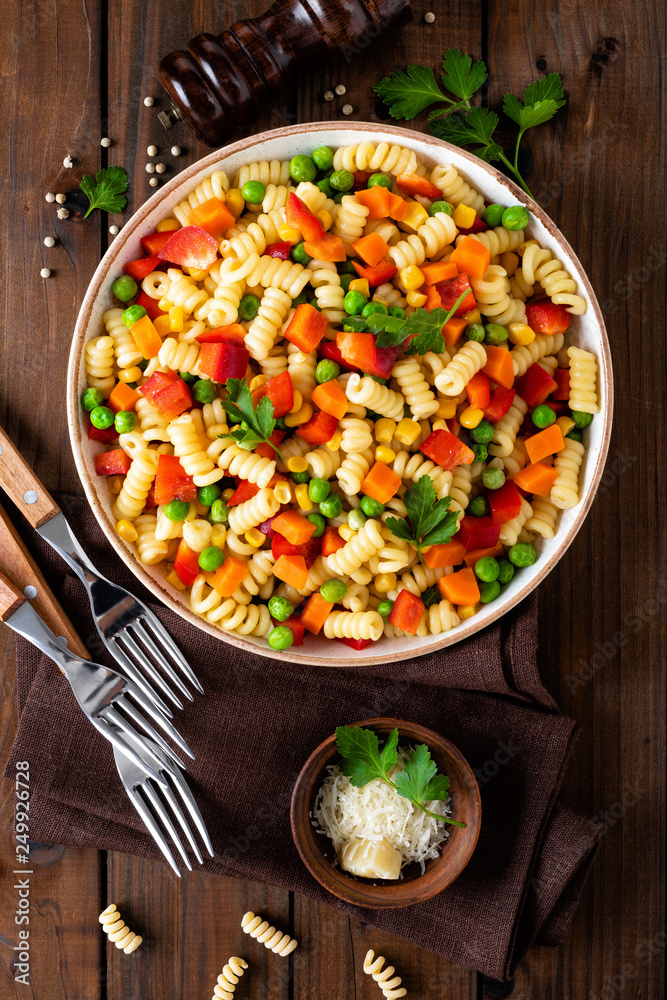 Italian pasta salad with fusilli, corn, boiled carrot, fresh green peas and sweet pepper on wooden rustic background. Top view Italian pasta salad with fusilli, corn, boiled carrot, fresh green peas and sweet pepper on wooden rustic background. Top view