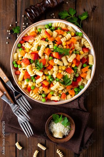 Italian pasta salad with fusilli, corn, boiled carrot, fresh green peas and sweet pepper on wooden rustic background. Top view