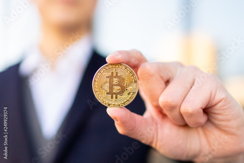 Bitcoin cryptocurrency coin in a young businessman hand. Disruptive blockchain technology concept and transfer of wealth.