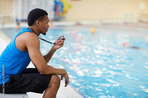 Side view portrait of handsome African-American fitness coach working in swimming pool, copy space