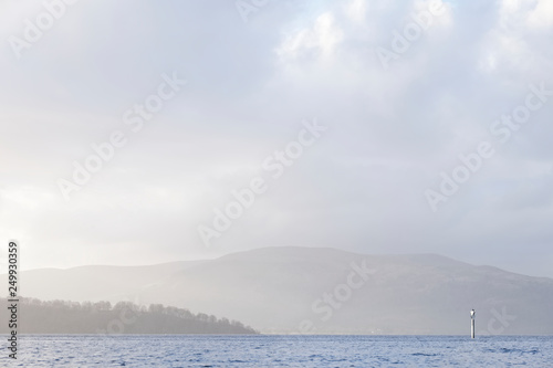 Calm peaceful atmospheric view of lake at Loch Lomond during change of weather from rain to sunshine