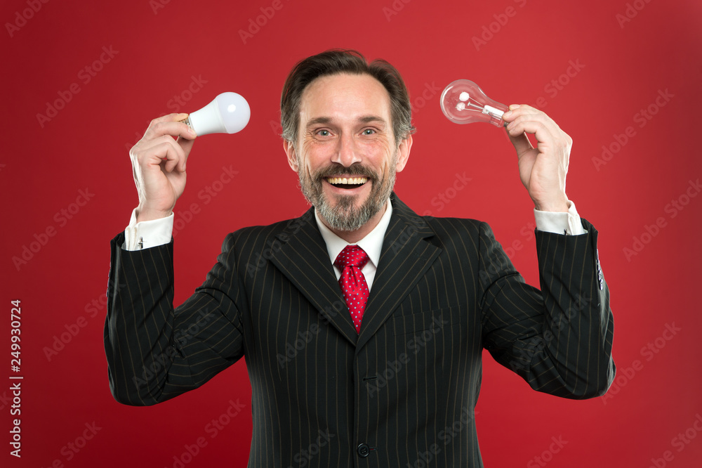 Energy efficient lighting. Lighting choices to save money. Man bearded consultant formal suit hold light bulb on red background. Symbol of idea progress and innovation. Environment friendly lighting Energy efficient lighting. Lighting choices to save money. Man bearded consultant formal suit hold light bulb on red background. Symbol of idea progress and innovation. Environment friendly lighting