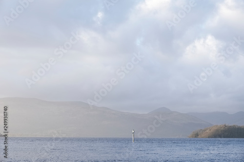 Calm peaceful atmospheric view of lake at Loch Lomond during change of weather from rain to sunshine