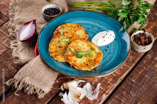 Close-up view of potato pancakes. Potato cake on a blue plate above a wooden table, with fresh parsley and sour cream.