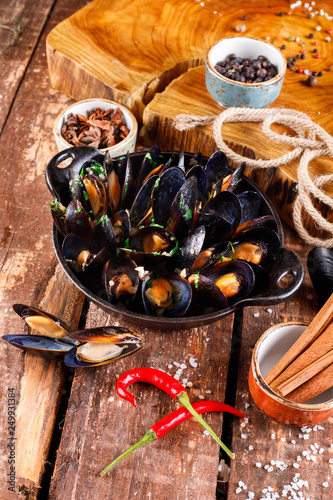 Boiled mussels in copper dish for cooking on wooden background, near rope and products for cooking