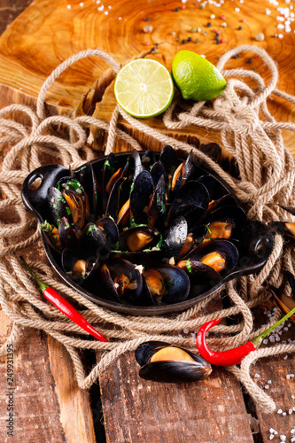 Boiled mussels in copper dish for cooking on wooden background, near rope and products for cooking