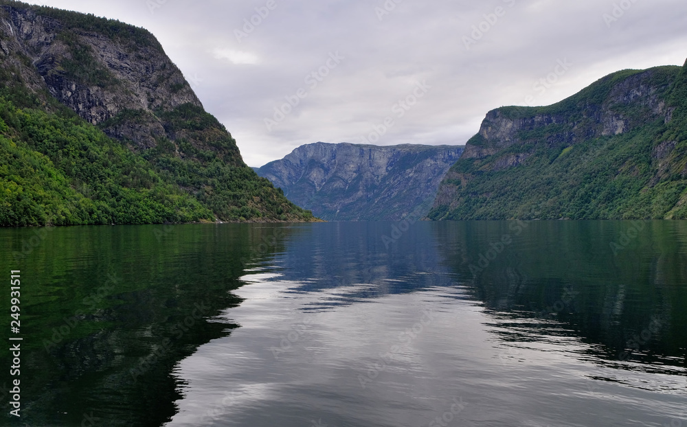 Holy grail illustrated from Sognefjord or Sognefjorden created from mountain range with blue sky and reflection in clear water and having a wooden dock point out in a river in Flåm