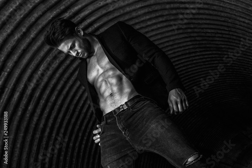 Muscular young man with beard on dark tunnel urban background. Fashion portrait of brutal strong muscle guy with modern trendy hairstyle. Model  fashion concept. Sexy naked torso. Black and white.