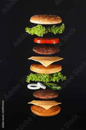 Flying burger ingredients. Delicious hamburger with flying ingredients on black background Flying burger ingredients .