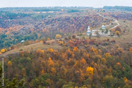 old orthodox church on a top of a hill, ancient cemetery on a cold, cloudy autumn day, yellow and red trees, pastoral landscpae background