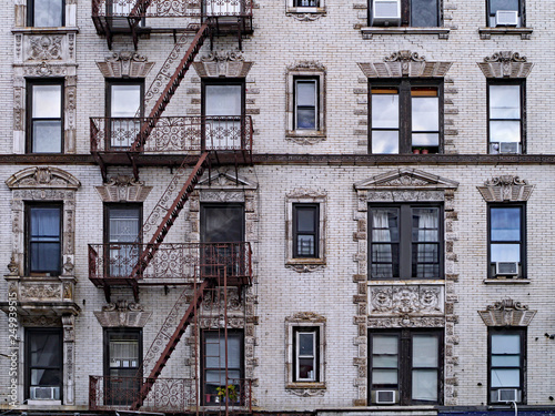 old New York apartment building with external fire escapes, window air conditioners, and ornate trim around windows