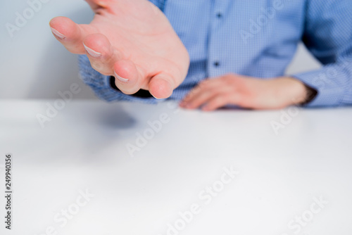 A man dressed in a blue shirt has his hands folded on the table. The businessman stretches out his hand, is upset by what he hears. Concept of failure in business.