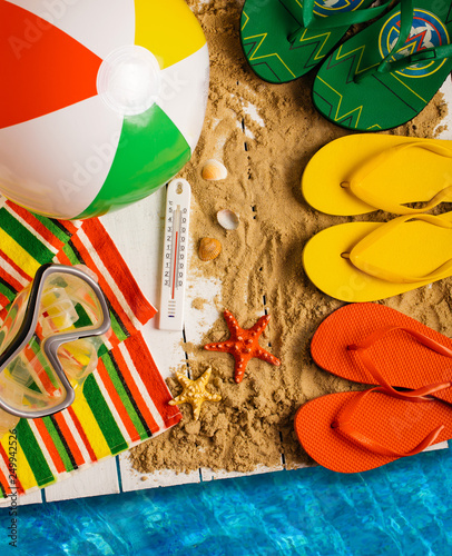 Flip flops, ball, tablet pc, seashell and starfish with tropical flowers on sandy beach
