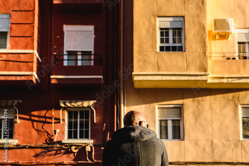 Black man, with shaved head, on his back and sitting in front of old buildings