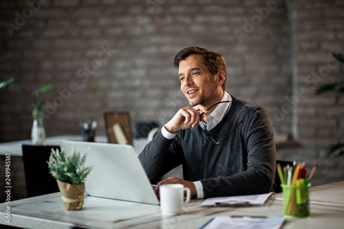 Smiling businessman day dreaming while working on laptop in the office. photo