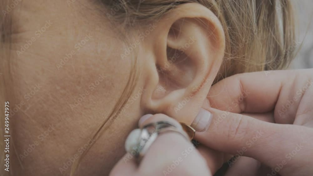 Close-up of female hands puting on handmade earrings outdoors.