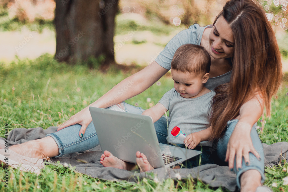 Mother with son sitting in the park and work on laptop. Mother with son sitting in the park and work on laptop.