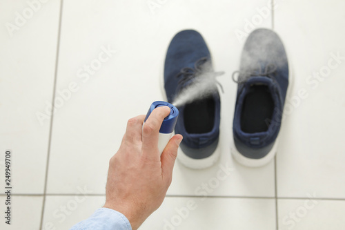 Man spraying deodorant over pair of shoes at home, closeup