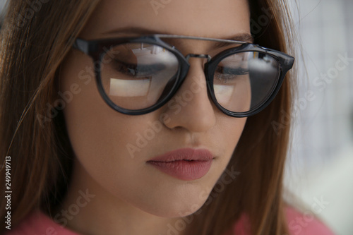 Young woman wearing glasses on blurred background, closeup. Ophthalmology service