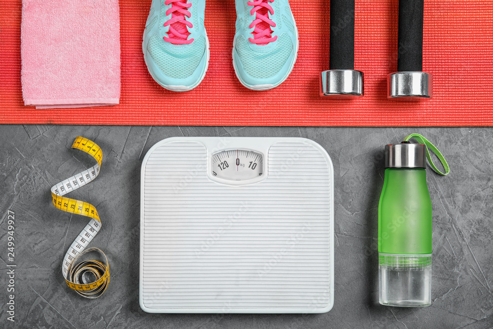 Flat lay composition with scales, measuring tape and sport equipment on gray background. Weight loss