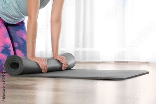 Woman rolling yoga mat on floor indoors, closeup. Space for text