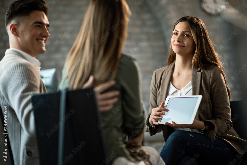 Smiling financial advisor using touchpad and showing the terms of loan to her clients. Smiling financial advisor using touchpad and showing the terms of loan to her clients.