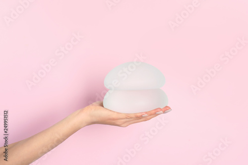 Woman holding silicone implants for breast augmentation on color background, space for text. Cosmetic surgery photo