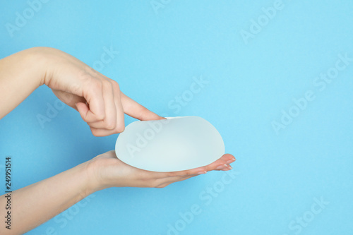 Woman touching silicone implant for breast augmentation on color background, space for text. Cosmetic surgery