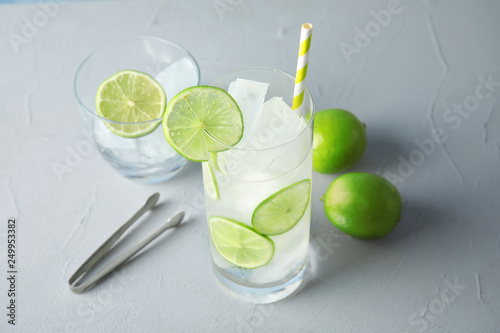 Glass of drink with lime and ice cubes on table