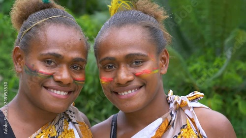 SLOW MOTION, PORTRAIT, CLOSE UP: Beautiful girls wearing traditional face paint and native outfits before a Melanesian ceremony. Lovely black friends wear vibrant make up and smile at the camera.