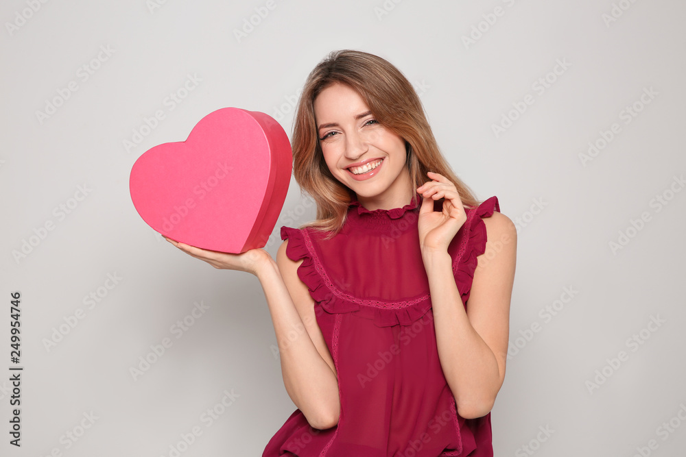 Portrait of beautiful smiling girl with heart shaped gift box on light background. International Women's Day Portrait of beautiful smiling girl with heart shaped gift box on light background. International Women's Day