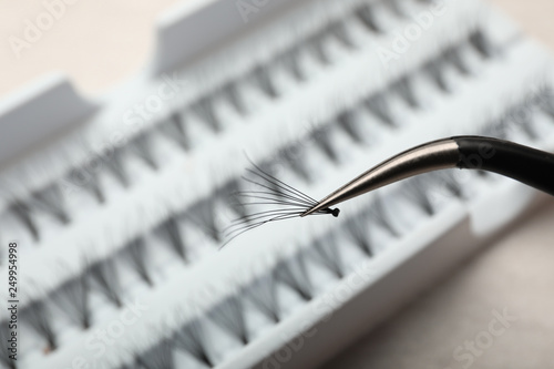 Tweezers with bunch of artificial eyelashes on blurred background, closeup. Space for text