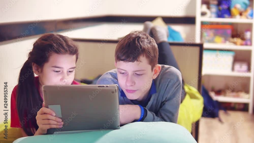 little boy and girl are playing and dog on the tablet lying on the bed. boy and girl teens social media internet on a tablet indoors. children and tablet concept lifestyle little boy and girl are playing and dog on the tablet lying on the bed. boy and girl teens social media internet on a tablet indoors. children and tablet concept lifestyle