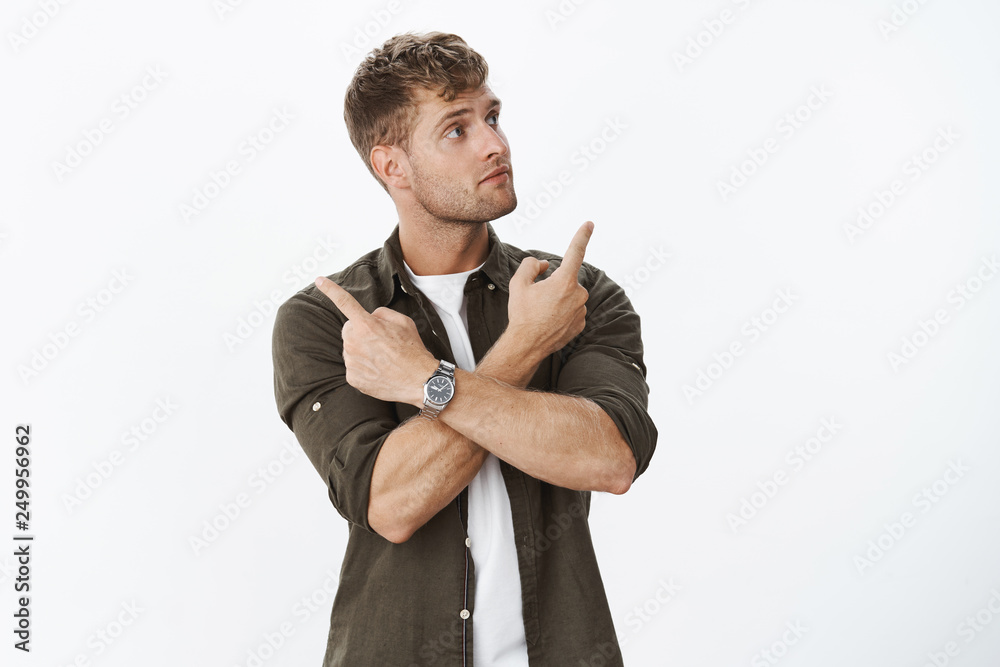 Guy making choice from various cool products, being intrigued with  something on right as cross hands over body pointing sideways, looking  unsure and curious taking decision over grey background Stock Photo |