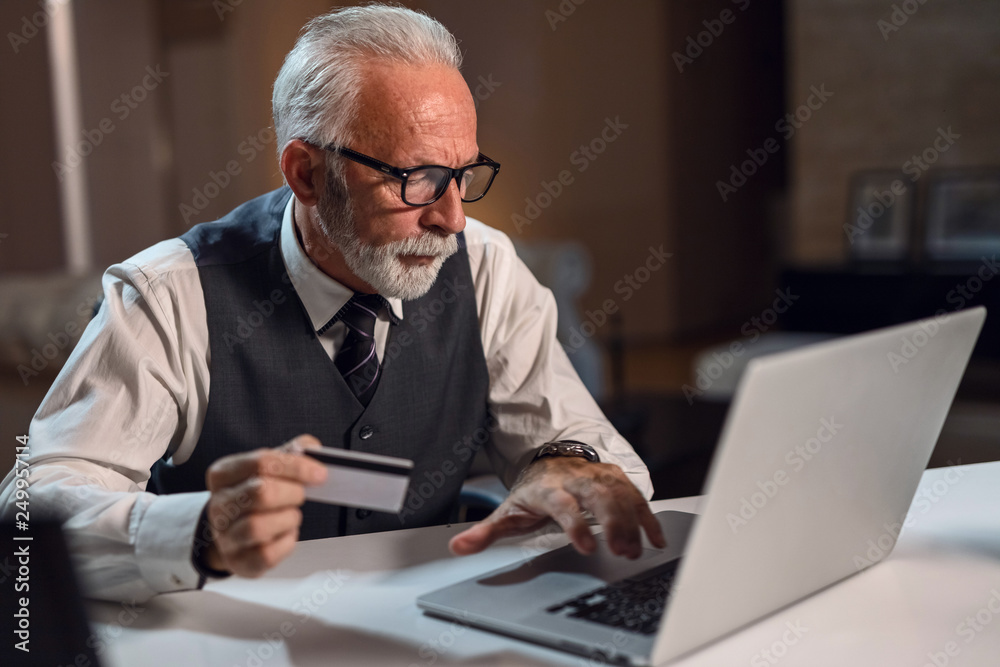 Senior businessman holding credit card while using laptop. Senior businessman holding credit card while using laptop.