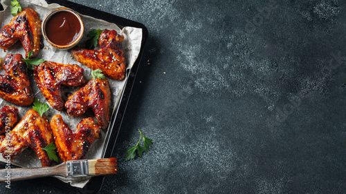 Roasted chicken wings in barbecue sauce with sesame seeds and parsley in a baking tray on a dark table. Top view with copy space. Tasty snack for beer on a dark background. Flat lay