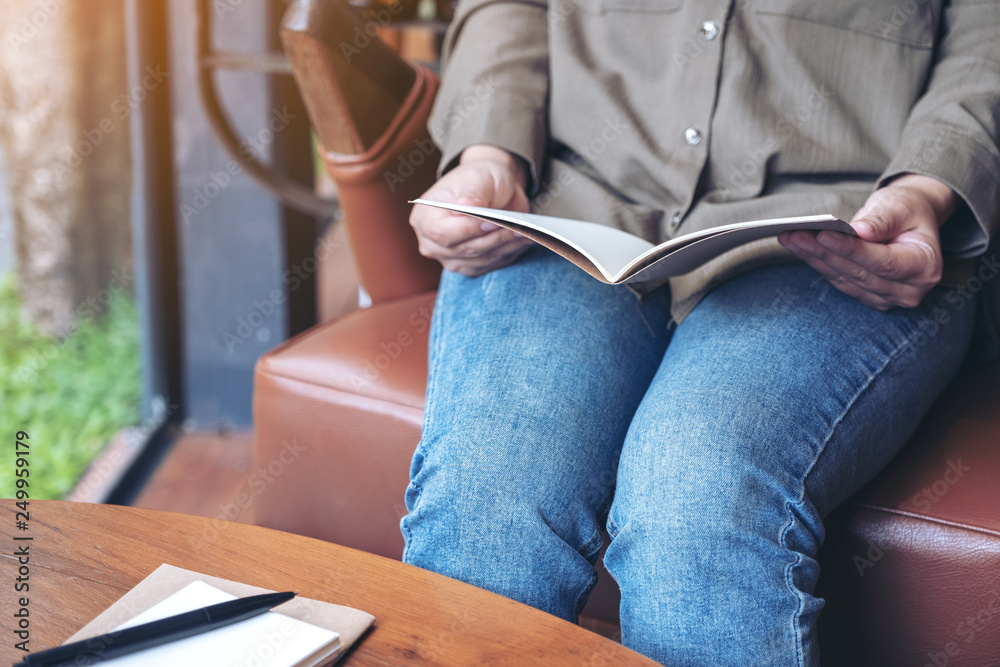 Obraz premium Closeup image of a woman opening a book to read with notebooks and coffee cup on wooden table in cafe