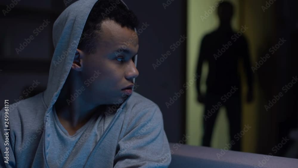 Scared african american teenager sitting in darkness male opening door, violence Scared african american teenager sitting in darkness male opening door, violence