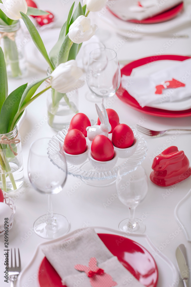 Happy easter. Decor and table setting of the Easter table is a vase with white tulips and dishes of red and white color. Easter colored eggs with white polka dots. Happy easter. Decor and table setting of the Easter table is a vase with white tulips and dishes of red and white color. Easter colored eggs with white polka dots.