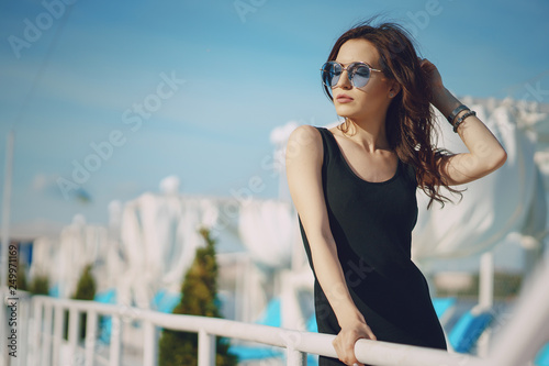 A beautiful young girl with curly hair and glasses standing by the water © prostooleh